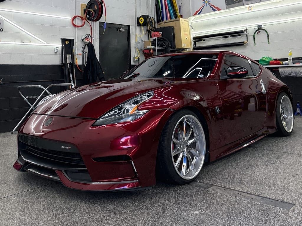 Deep candy red Nissan 370Z Nismo with chrome wheels inside the shop