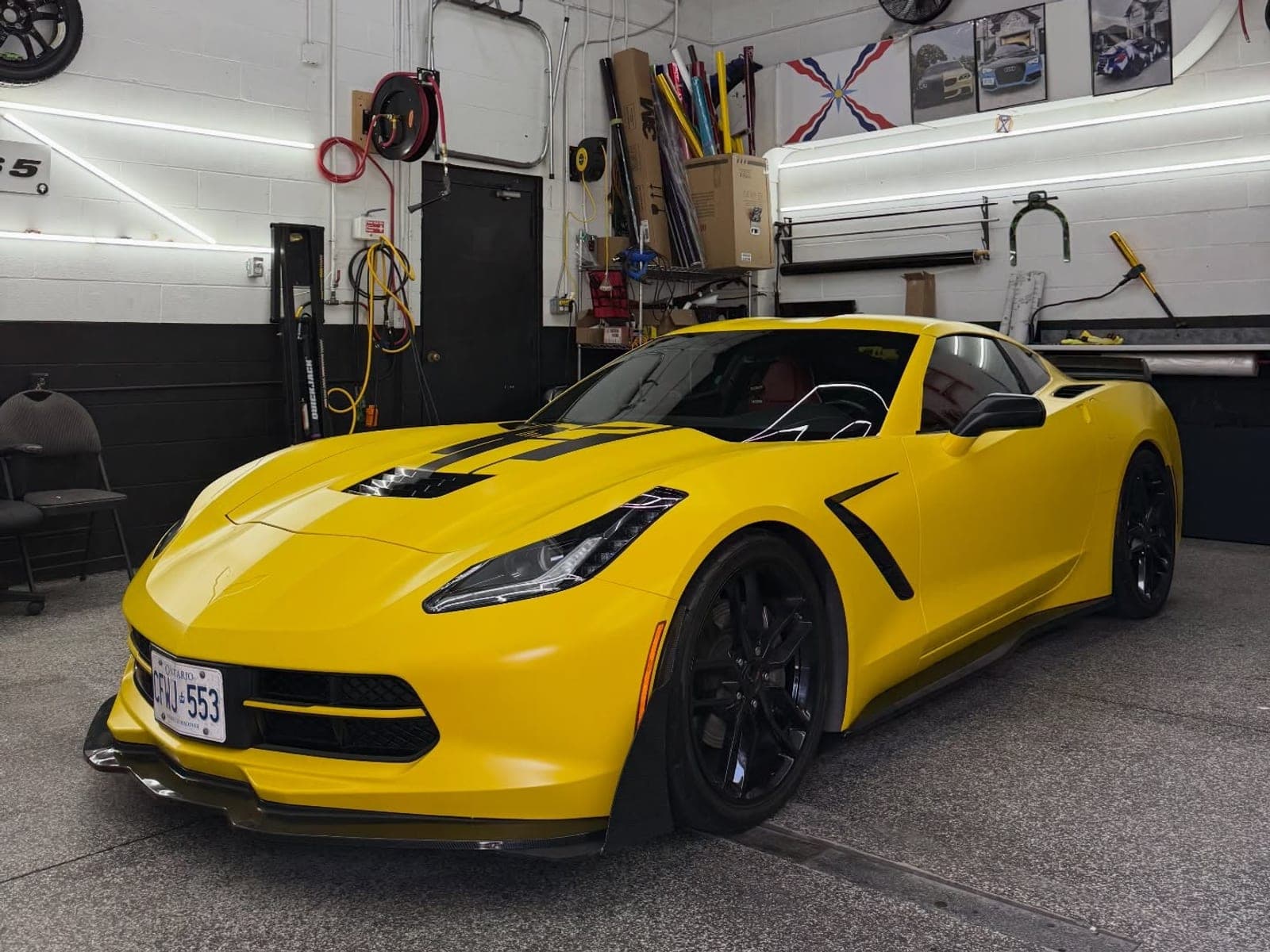 Satin yellow Chevrolet Corvette C7 with black wheels and accents inside the shop
