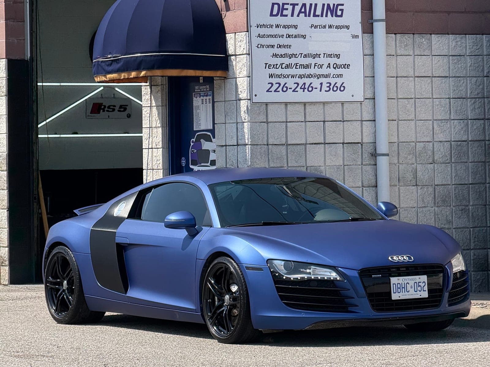 Matte metallic blue Audi R8 with black side blades in front of the WrapLab bay door