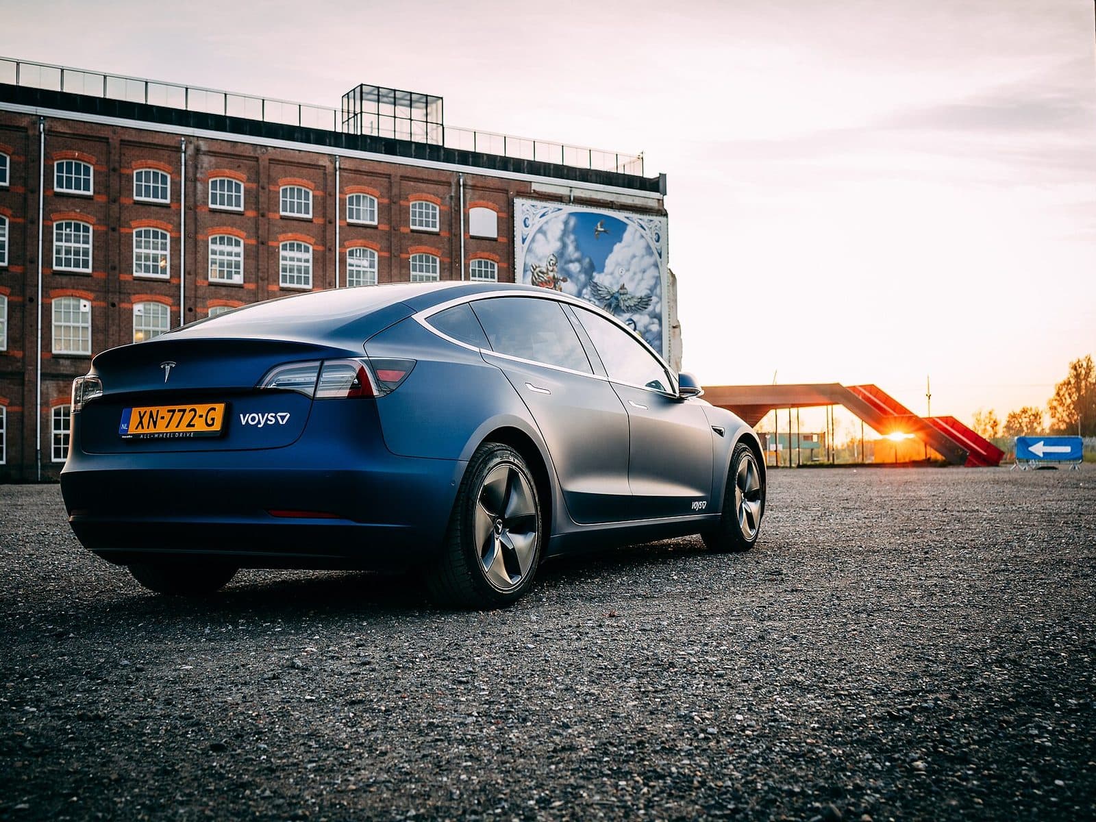 Blue wrapped company Tesla Model 3 outside a brick building at sunset